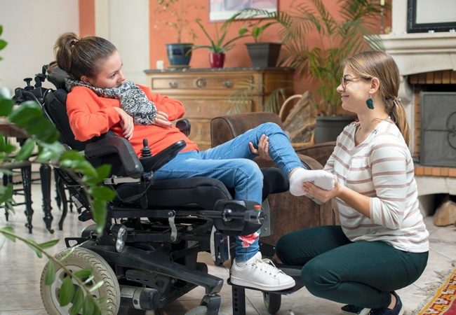 Aide à domicile qui détend les jambes d'une femme handicapé