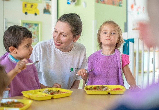 Aide ADMR qui aide des enfants à manger à la crèche