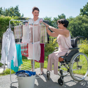 Aide à domicile aide une personne en fauteuil à étendre son linge sur sa terrasse