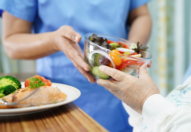 Aide à domicile qui donne une salade composée à une dame âgée