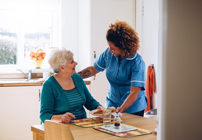 Aide à domicile souriante qui apporte une assiette à une dame âgée heureuse