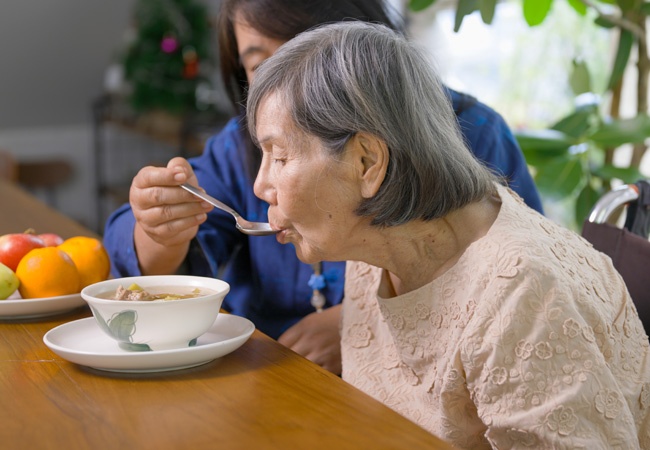 Aide qui fait manger une dame âgée