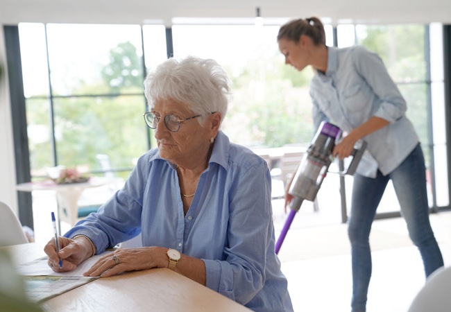 Aide qui passe l'aspirateur chez une dame âgée