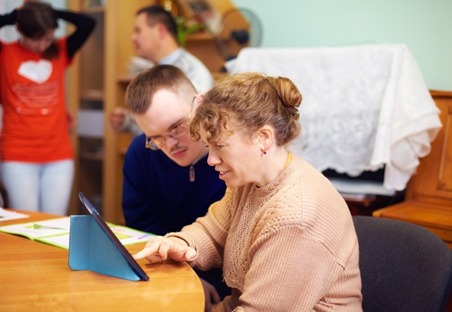 Dame qui aide un homme en situation de handicap à utiliser une tablette