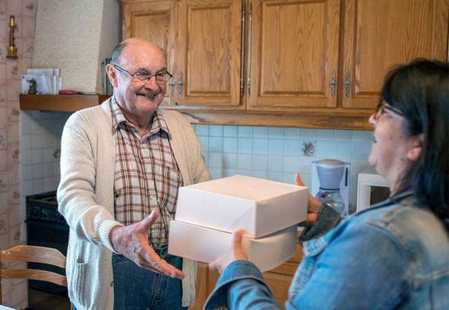 Dame qui donne des boites repas à un monsieur âgé dans sa cuisine