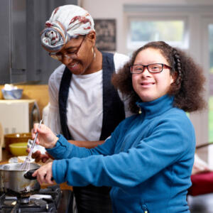 Dame souriante qui aide une personne trisomique à cuisiner