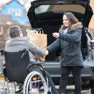 Femme qui aide un homme en fauteuil à mettre ses courses dans sa voiture