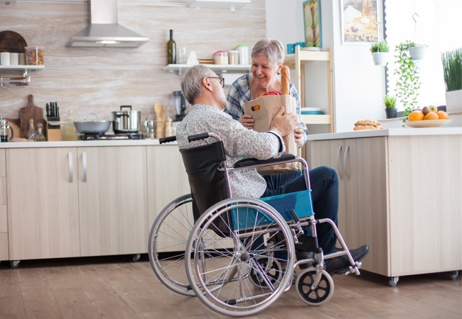 Femme qui aide un homme en fauteuil à ranger ses courses dans sa cuisine