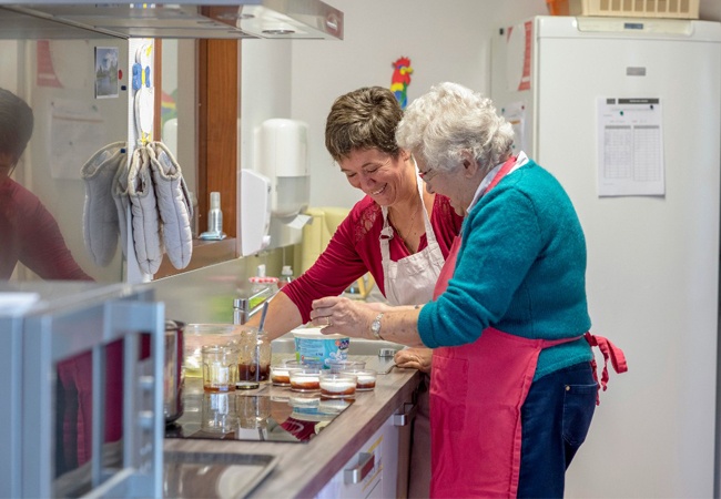 femme souriante qui aide une dame âgée à cuisiner dans sa cuisine