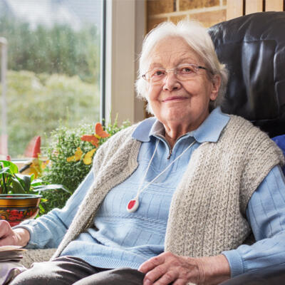 Femme âgée souriante avec un collier téléassistance assise dans son canapé