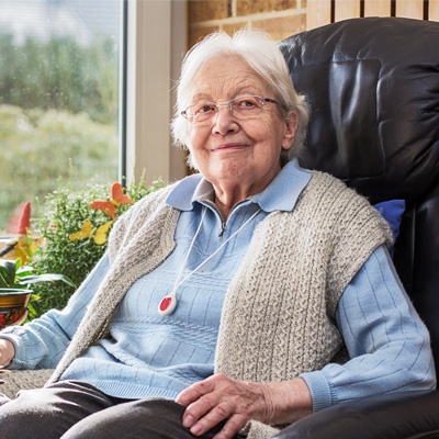 Femme âgée souriante avec un collier téléassistance assise dans son canapé