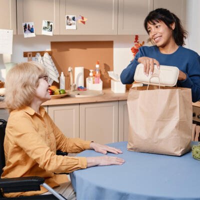 Femme souriante qui apporte le repas à une dame en fauteuil