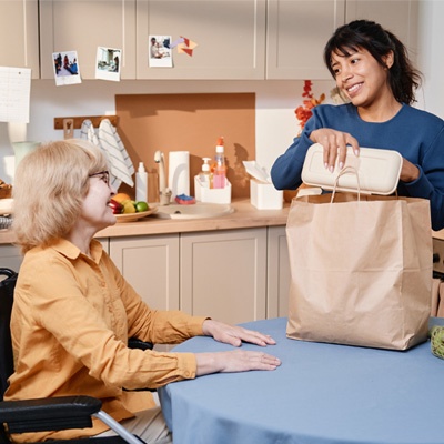 Femme souriante qui apporte le repas à une dame en fauteuil