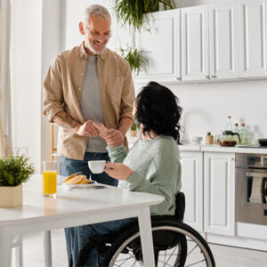 Homme souriant qui aide une femme en fauteuil à prendre son petit déjeuner