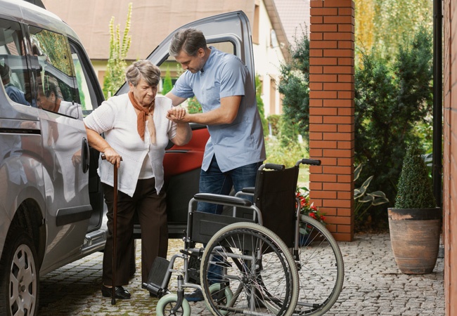 soignant qui aide une dame à sortir de la voiture