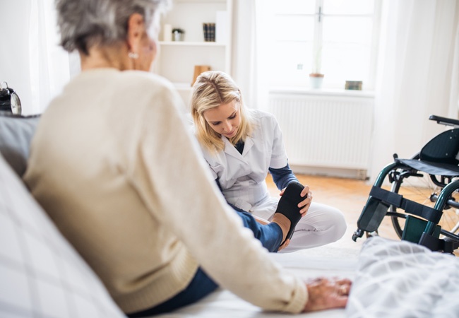 Une infirmière aide une personne en fauteuil à mettre ses chaussures