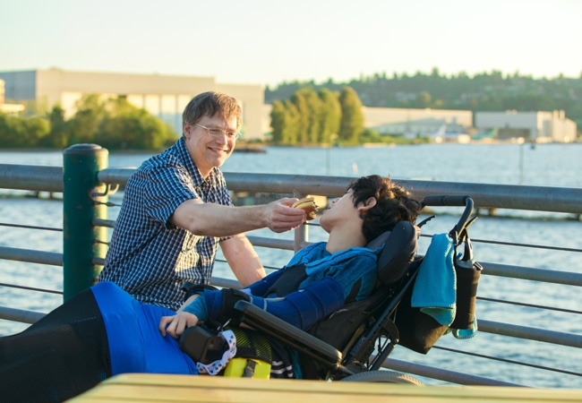 Un homme fait manger une personne en situation de handicap au bord de l'eau