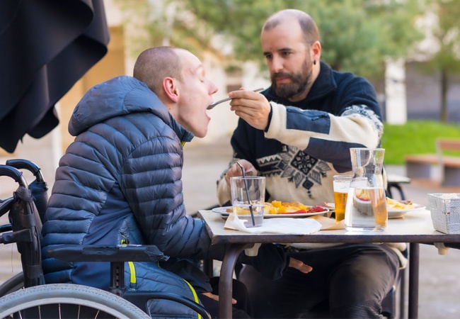 Un homme fait manger une personne en situation de handicap au restaurant