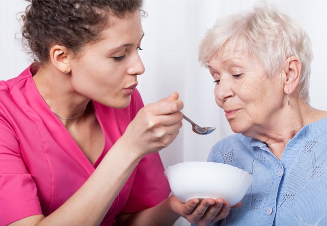 Une aide à domicile donne à manger à une dame âgée