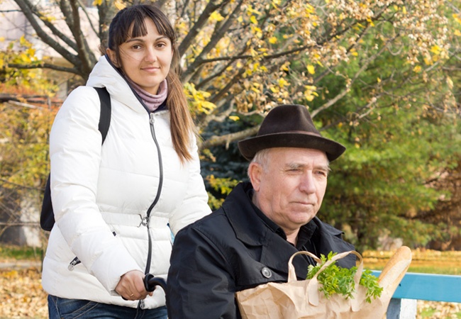 Une femme qui pousse un homme en fauteuil qui tient ses courses