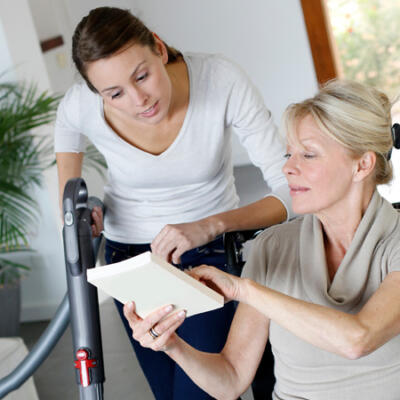 Une femme souriante passe l'aspirateur chez une dame en fauteuil roulant