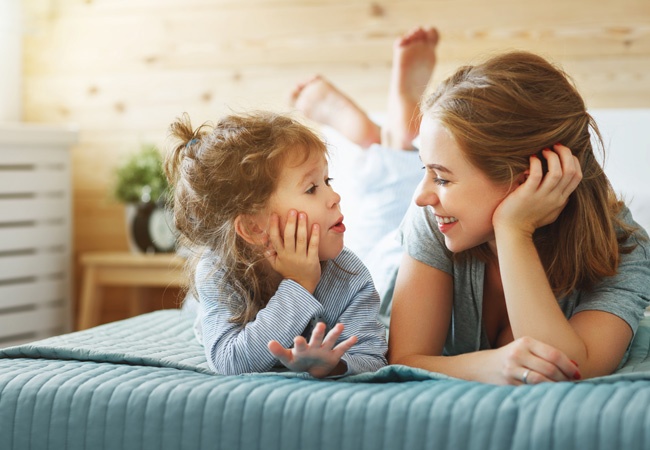 Une petite fille et une aide à domicile étendues sur un lit qui discutent