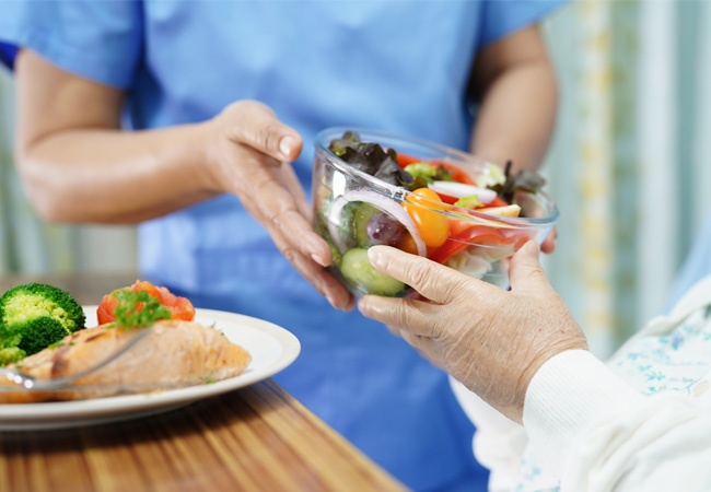 aide à domicile qui donne une salade composée à une femme âgée