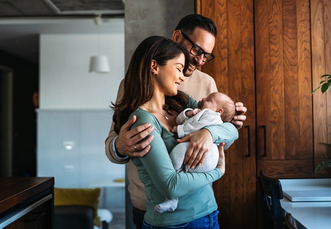 couple qui sourit à leur nouveau né en se serrant dans les bras