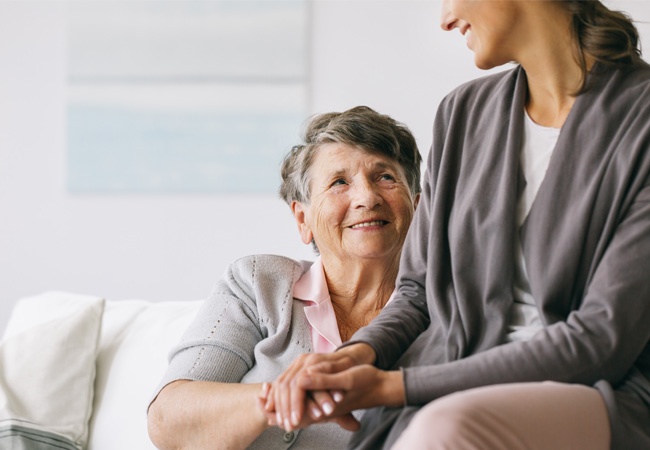 dame qui tient la main à une femme âgée et elles se sourient