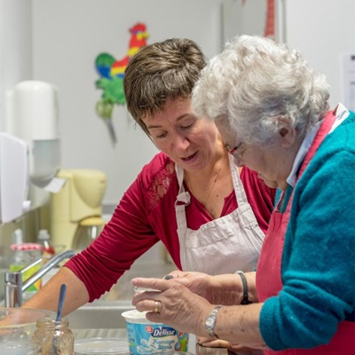 femme souriante qui aide une dame âgée à faire des yaourt